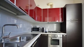 A modern kitchen with stainless steel appliances, a double sink, and red cabinets. - Trilo Mina 3 in Gabicce Mare (Cattolica)