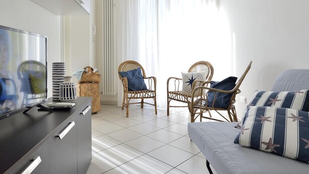 A modern living room with a flat-screen TV, wicker chairs, a grey sofa, and a tiled floor. - Trilo Mina 3 in Gabicce Mare (Cattolica)