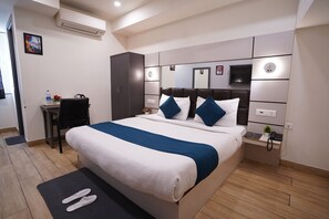 Ein modernes Hotelzimmer mit einem großen Bett, einem Schreibtisch, einem Sessel und einem kleinen Tisch mit Telefon und Pflanze.