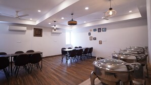 Un salón de conferencias con una mesa larga, sillas, ventiladores de techo y unidades de aire acondicionado instaladas en las paredes.