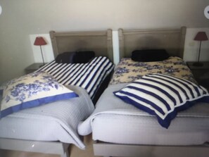 Two beds with unique headboards and pillow designs, each with a patterned bedspread and matching pillow, are arranged in a cozy setup.