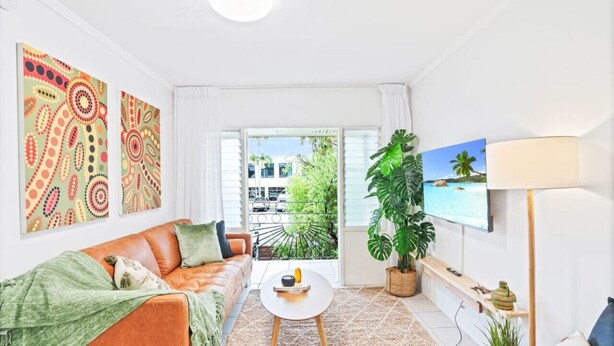 Una sala de estar luminosa con un sofá, una mesa de centro, un televisor y un ventanal con vistas al exterior.