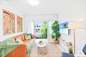 A bright living room with a sofa, a coffee table, a TV, and a large window with a view of the outside.