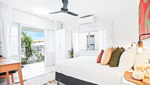 Un dormitorio con cama, escritorio, ventilador de techo y ventana con cortinas.