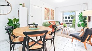 Una sala moderna con una mesa de comedor redonda de madera, sillas negras, un sofá y una mesa de centro. Hay plantas en macetas y obras de arte en las paredes.