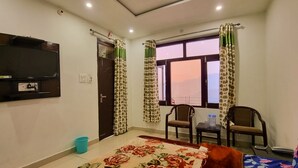 Una habitación con cama, televisión montada en la pared, dos sillas, una mesita y una ventana con cortinas.