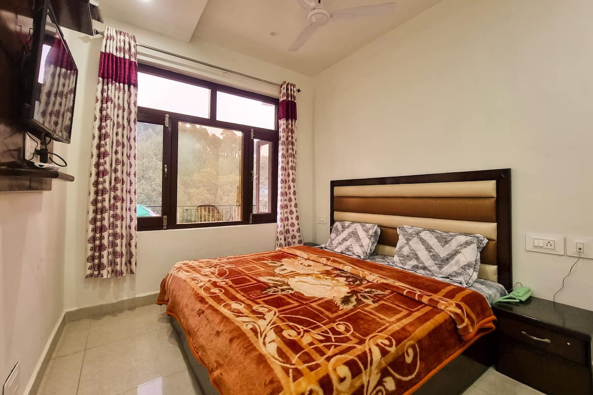 A bedroom with a bed, a nightstand, a TV, and a window with curtains.