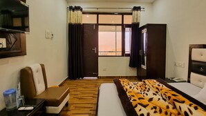 Habitación de hotel con cama, una silla, escritorio con teléfono, televisor y ventana con cortinas.