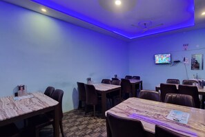 Un salón de conferencias con varias mesas y sillas, un ventilador de techo y un televisor montado.