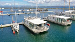 A marina with several boats docked, including a modern houseboat with a covered deck and outdoor seating area.