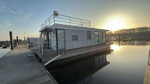 A modern floating structure with a flat roof, railings, and a dock extending into calm water.