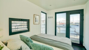 A bedroom with a bed, a window with a view of a marina, and a door leading outside.