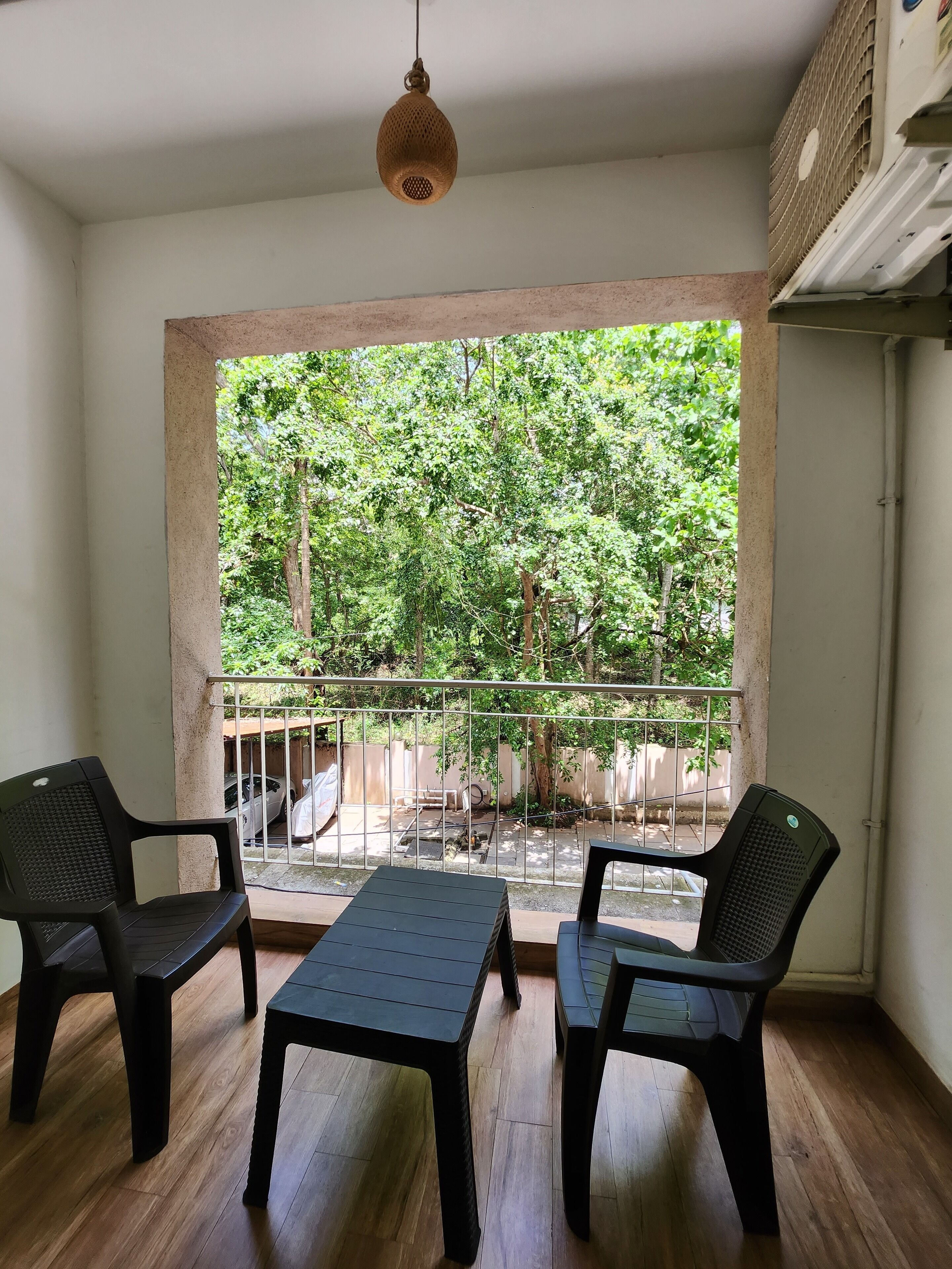 A balcony with a view of a garden, two chairs, a table, and a hanging light fixture.