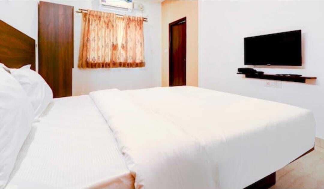 A hotel room with a bed, a television mounted on the wall, and a window with curtains.