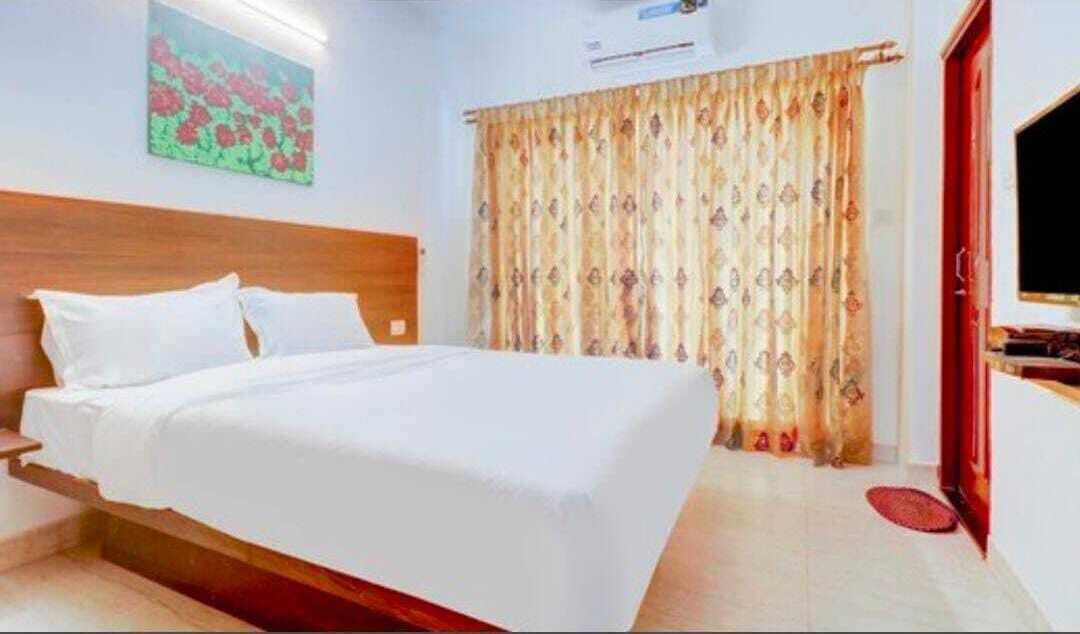 A hotel room with a bed, a wooden headboard, a painting on the wall, a curtain, and a television.
