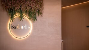 Een muur met een rond, verlicht bord waarop 'isabel's' staat en bloemrijke decoraties.