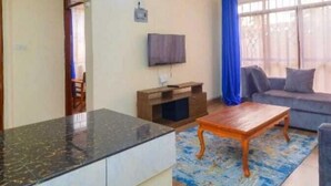 A living room with a sofa, a coffee table, and a TV mounted on the wall. - Lux Suites Juniours Apartment Bamburi (Mombasa)