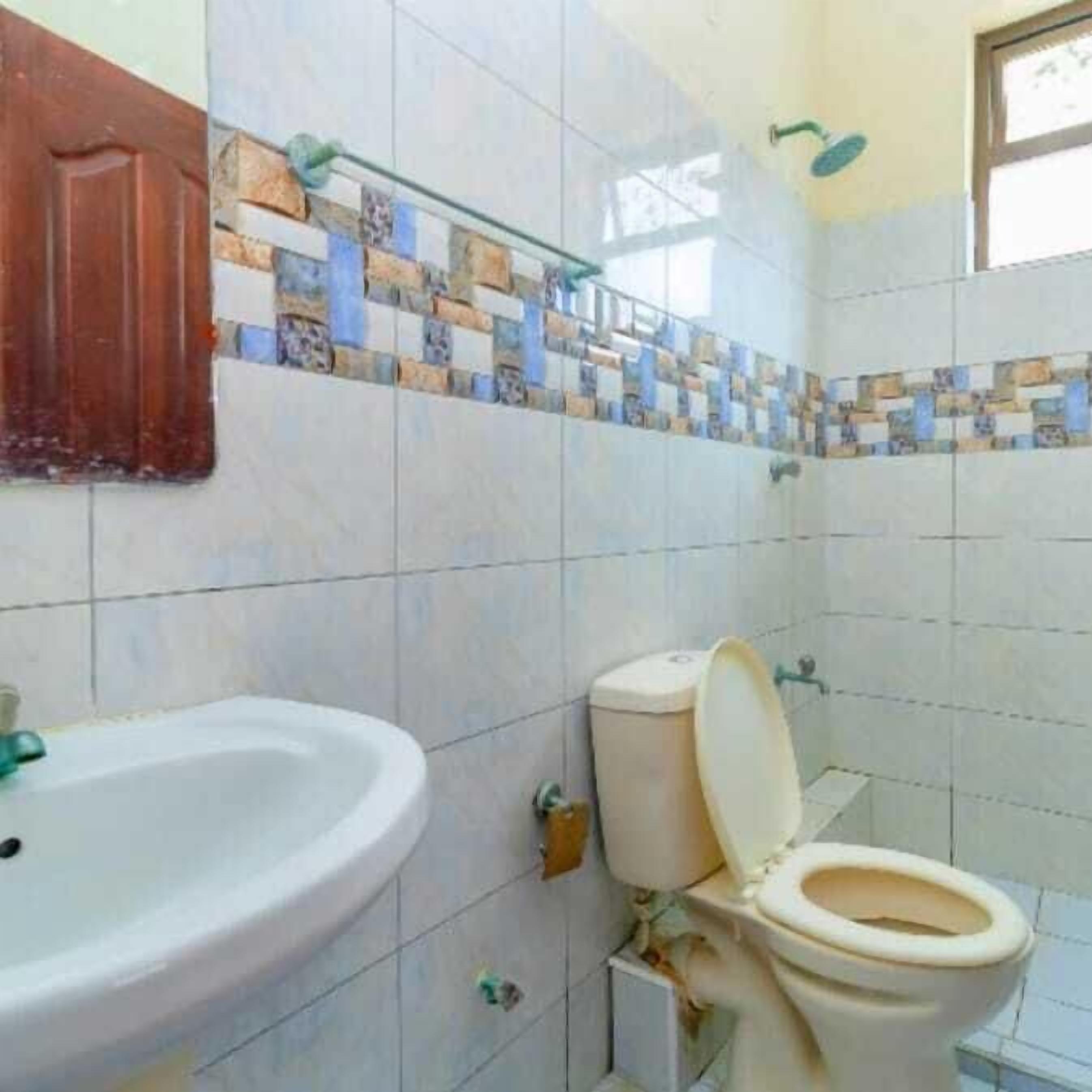 A bathroom with a tiled wall, a sink, and a toilet.