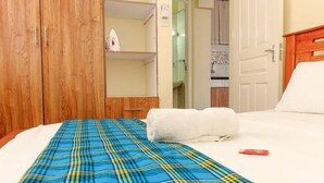 A hotel room with a plaid bedspread, a wooden wardrobe, and a white door. - Lux Suites Juniours Apartment Bamburi (Mombasa)
