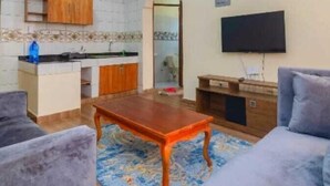 A living room with a wooden coffee table, a sofa, and a TV on the wall. - Lux Suites Juniours Apartment Bamburi (Mombasa)
