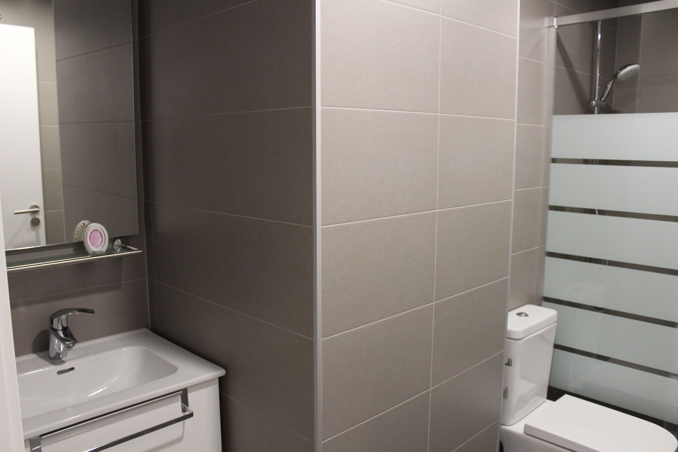 Un baño moderno con lavamanos, espejo y retrete blancos.