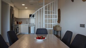 A modern kitchen with white cabinets, a stainless steel refrigerator, and a microwave. There is a dining table with a bowl of strawberries in the center. - Idillic penthouse between sea and pine trees (Salou)