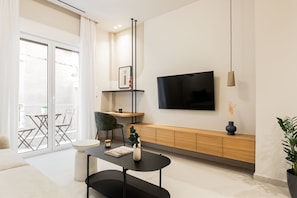 A modern living room with a flat-screen TV, a coffee table, a chair, and a potted plant.