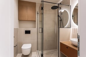 A modern bathroom with a glass-enclosed shower, a white toilet, and a wooden vanity with a sink.