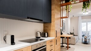 Une cuisine moderne équipée d’une cuisinière intégrée, d’une machine à café et d’un grille-pain. On y trouve un meuble en bois avec une poignée noire et un plan de travail blanc.