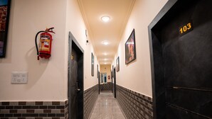 Un pasillo con extintor, puerta número 103 y cuadros en las paredes.