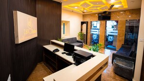 Zona de recepción de un hotel con diseño moderno, que incluye un mostrador de recepción, un área de estar y una pantalla grande que muestra el nombre del hotel.