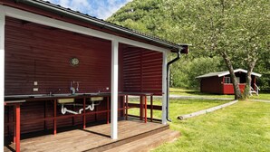 A red barn with a covered outdoor area, a wooden deck, and a small red building in the background.