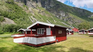 A red and white cabin with a porch, set against a mountainous backdrop.