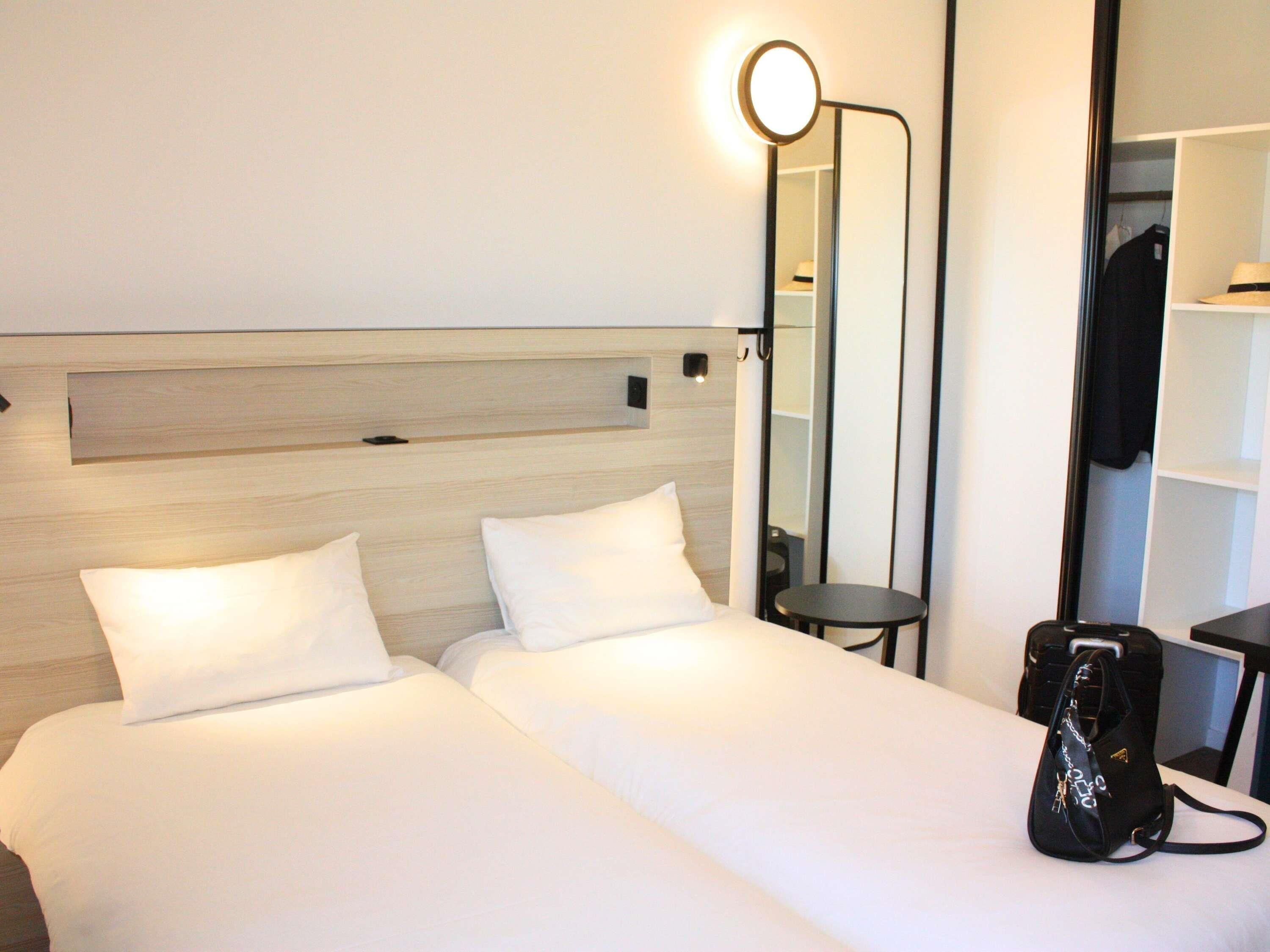 A hotel room with two beds, a bedside table, a mirror, and a wardrobe.