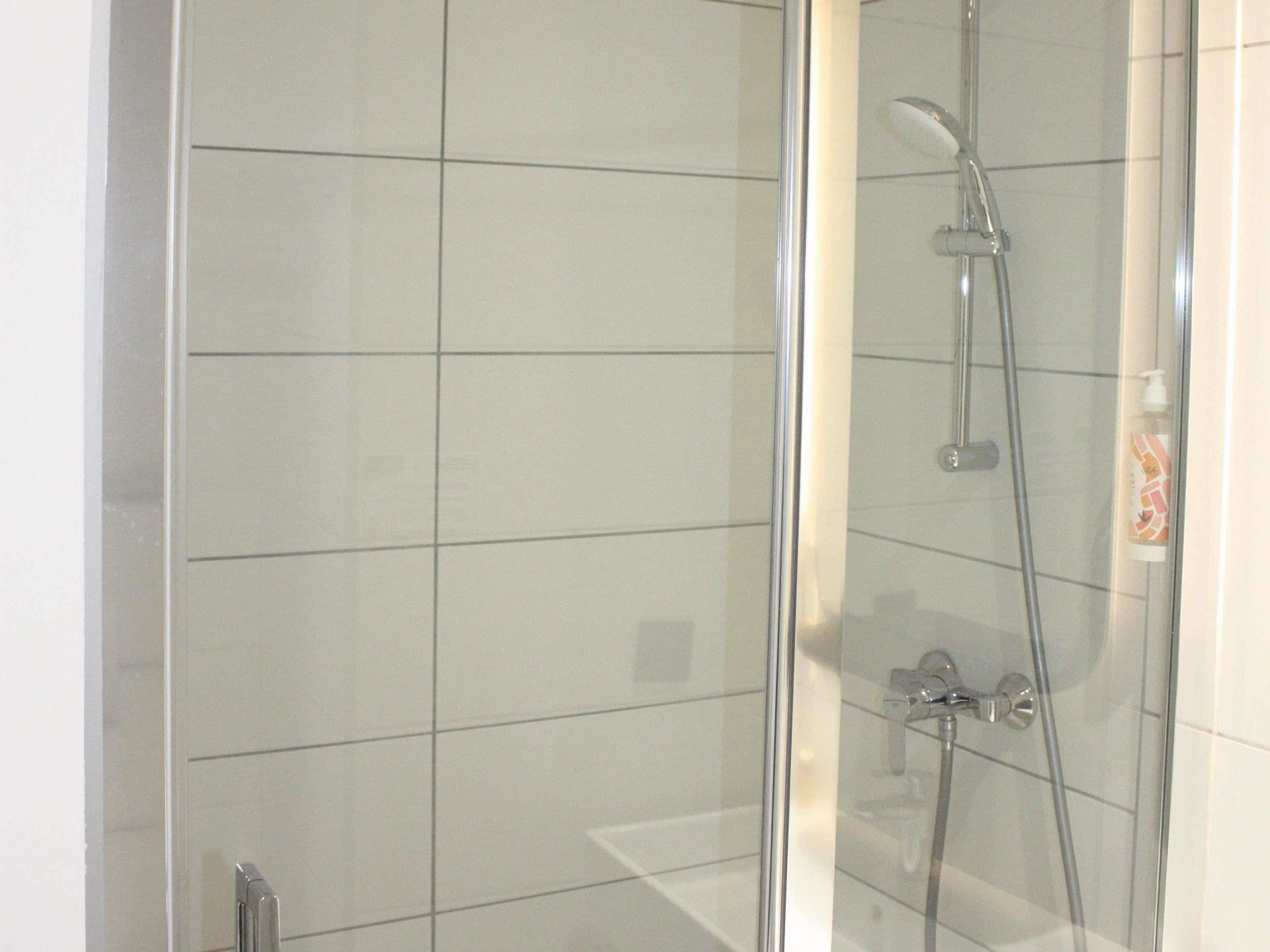 Een douche met glazen wand, een handdouche en een wandmengkraan.
