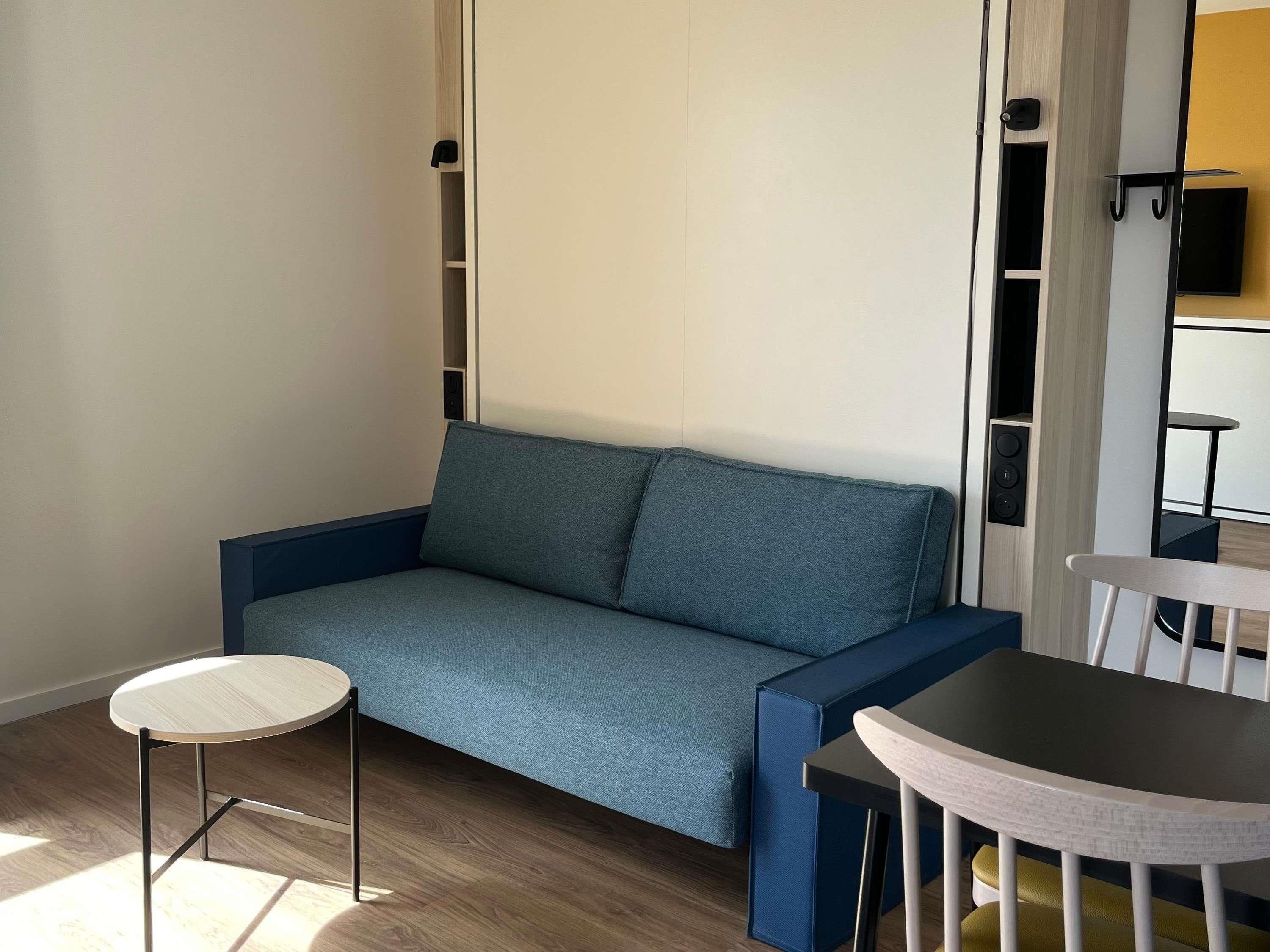 Une pièce moderne avec un canapé bleu, une petite table ronde et une chaise.