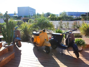 Une terrasse en bois oĂč sont garĂ©es trois vieilles scooters.