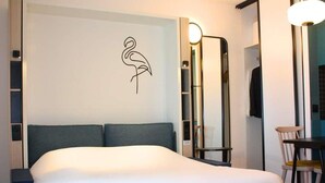 A modern hotel room with a bed, a mirror, a chair, and a wall-mounted artwork. - Aparthotel Adagio Access Porte De Camargue (Saint-Martin-de-Crau)
