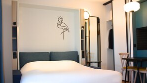 A modern hotel room with a bed, a chair, a table, and a wall-mounted light fixture. - Aparthotel Adagio Access Porte De Camargue (Saint-Martin-de-Crau)