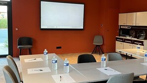 A conference room with a large table, chairs, a projector screen, and a kitchenette. - Aparthotel Adagio Access Porte De Camargue (Saint-Martin-de-Crau)