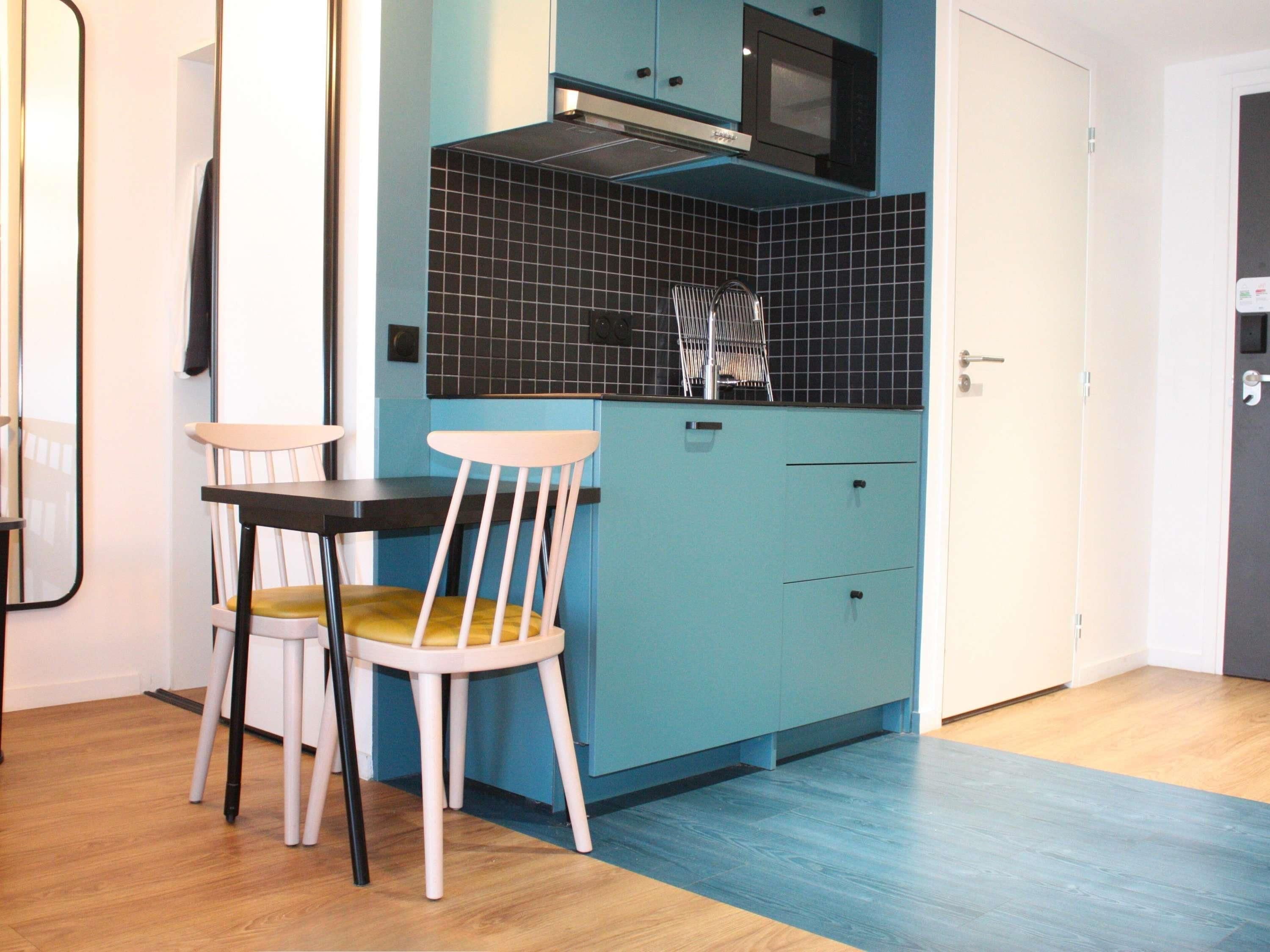 A kitchen with teal cabinets, a microwave, and two chairs with yellow cushions.