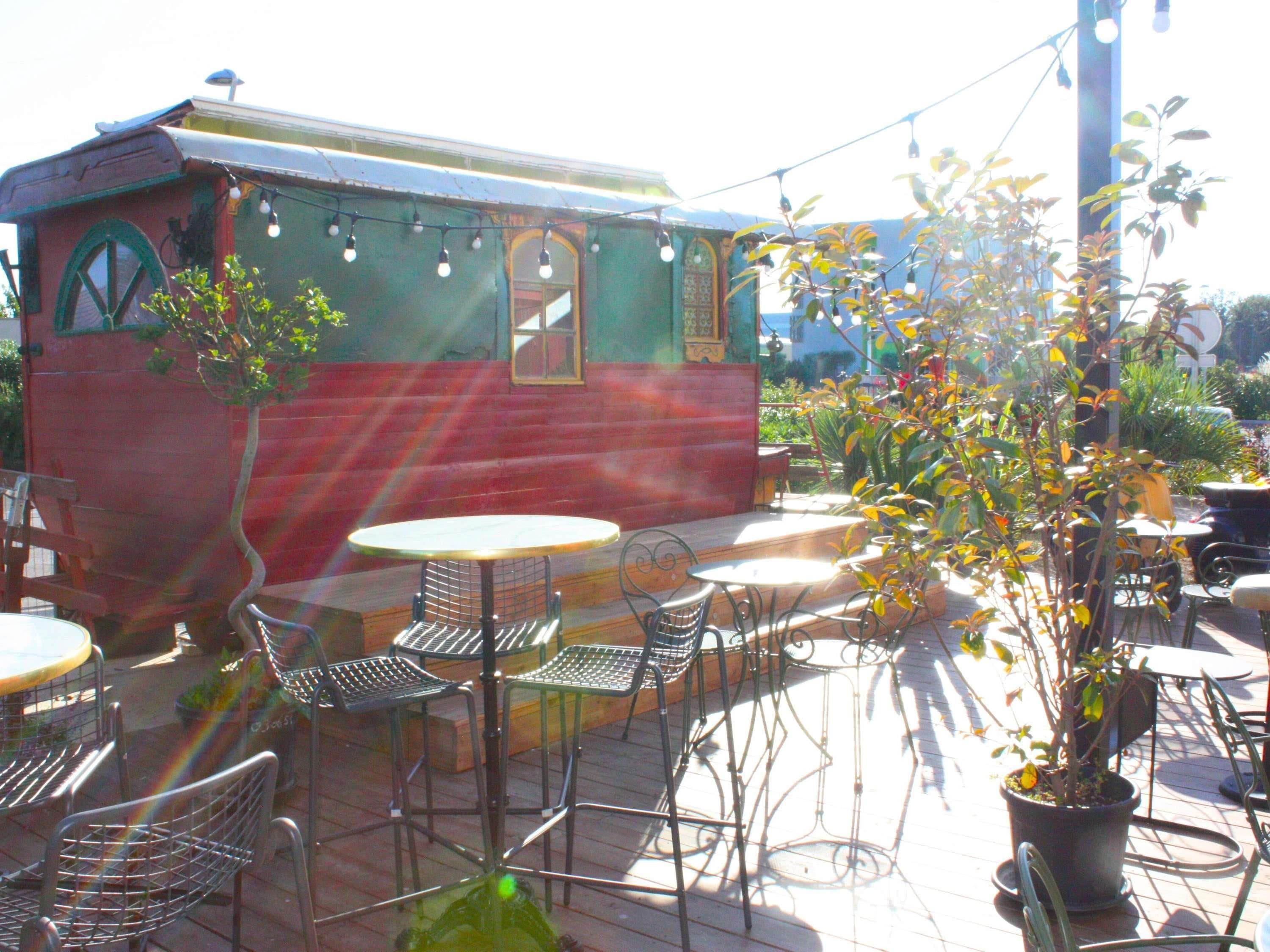 An outdoor seating area with tables and chairs, a potted plant, and a building with a green and red facade.