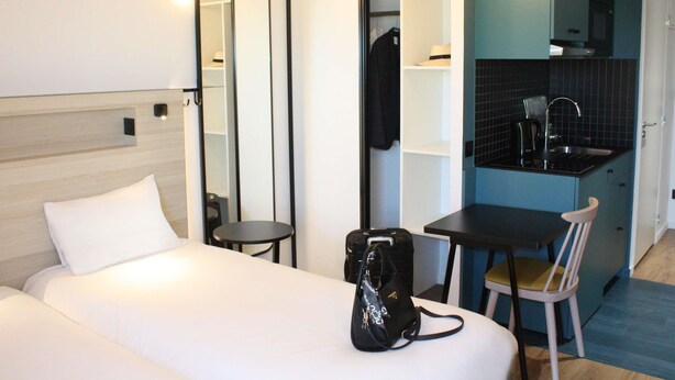 A hotel room with a bed, a small table, a chair, a desk, a kitchenette, and a mirror. - Aparthotel Adagio Access Porte De Camargue (Saint-Martin-de-Crau)