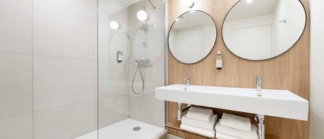 A modern bathroom with a glass shower enclosure, a white sink with a wooden vanity, and two round mirrors.