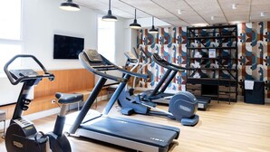 Een sportschool met fitnessapparatuur, een televisie en een decoratieve wand.