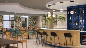 Een modern café met houten en zwarte barstoelen, een gebogen toonbank en een blauwe kast met flessen.