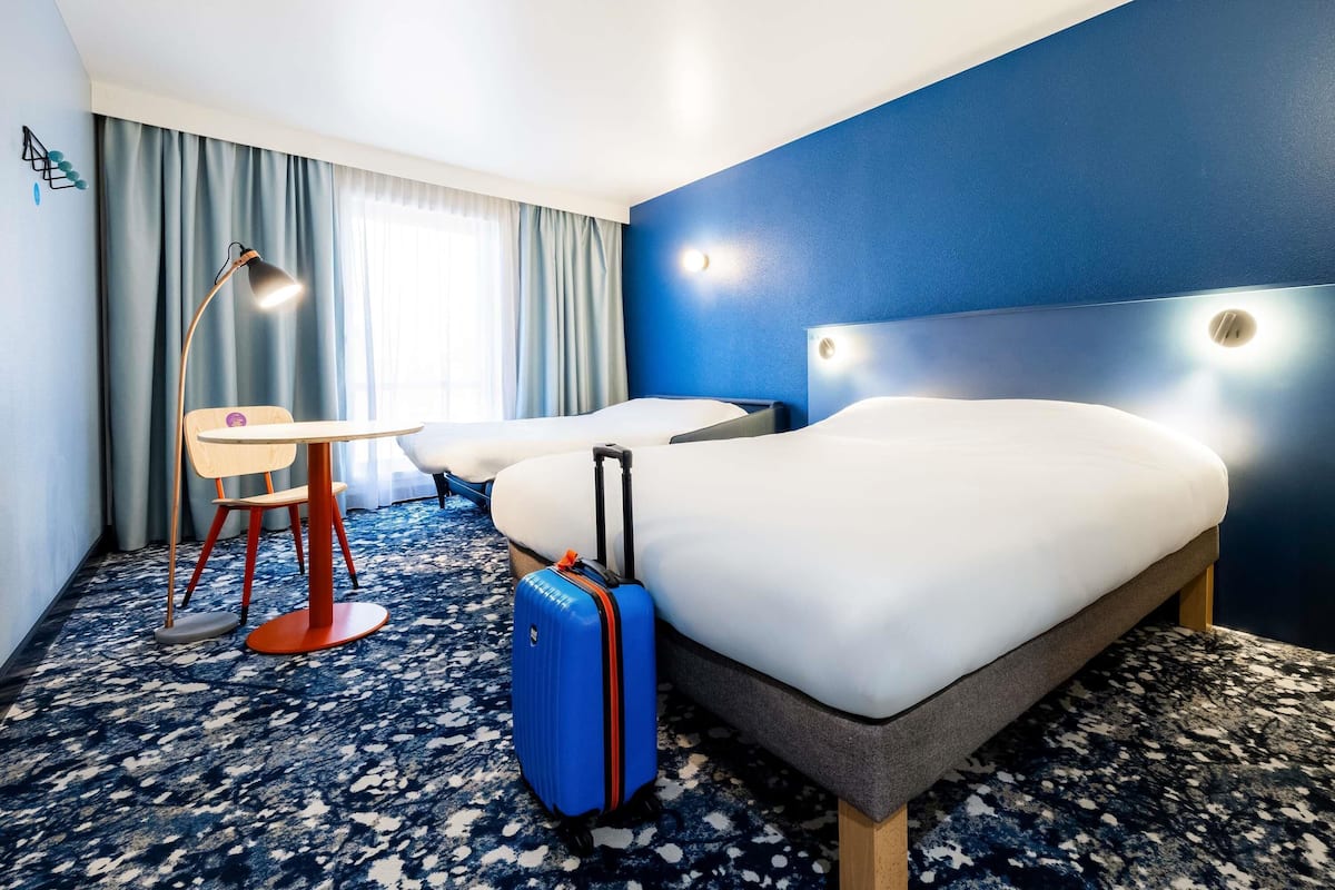 Een hotelkamer met een bed, bureau, stoel, koffer en een raam met gordijnen.