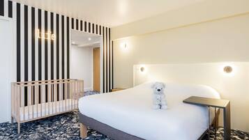 Une chambre d’hôtel avec un lit, un berceau, un ours en peluche et un mur à rayures verticales.