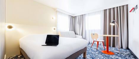 A hotel room with a large bed, a desk with a chair, a laptop, and a desk lamp.