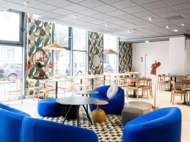 Interior de una cafetería moderna con asientos azules, mesas de madera y paredes con diseños.